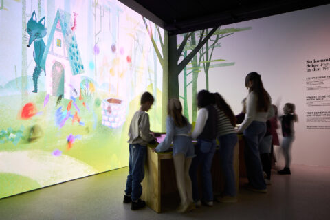 04 | IMMERGRUEN | © GRIMMWELT Kassel | Foto: Nicolas Wefers Kinder stehen im Raum an den Stempelstationen und erstellen mit virtuellen Stempeln eigene Figuren