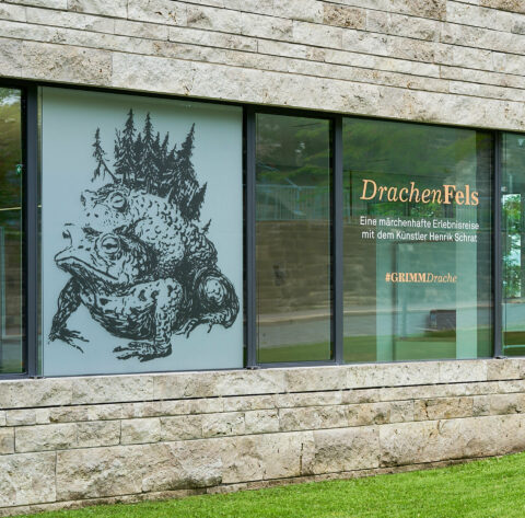 DrachenFels | Foto: Nikolaus Frank Zwei Kröten und Titel der Erlebnisreise auf einer Fensterscheibe der Büros der GRIMMWELT