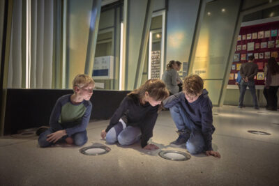 V | VOLKSMÄRCHEN | Kinder im Bereich VOLKSMÄRCHEN | Foto: Nikolaus Frank Kinder sitzen auf dem Boden im Ausstellungsbereich VOLKSMÄRCHEN.