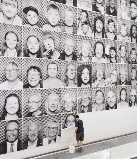 Inside Out Project, Kassel, 2025 | © GRIMMWELT Kasse | Nicolas Wefers Bilder von Besucherinnen und Besuchern an einer Wand im inneren der Grimmwelt