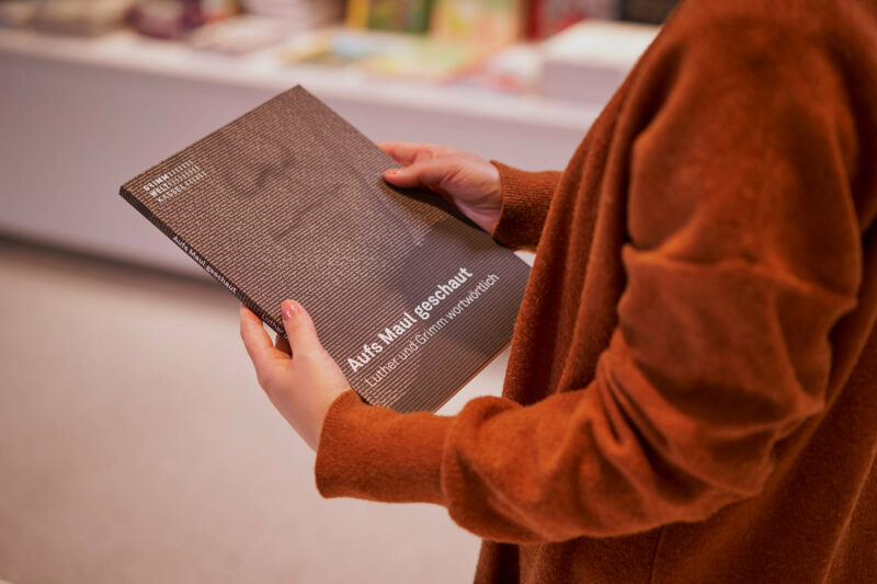 GRIMMWELT | Sonderausstellung | Publikation Aufs Maul geschaut | Foto: Nikolaus Frank Jemand hält die Publikation Aufs Maul geschaut in Händen.