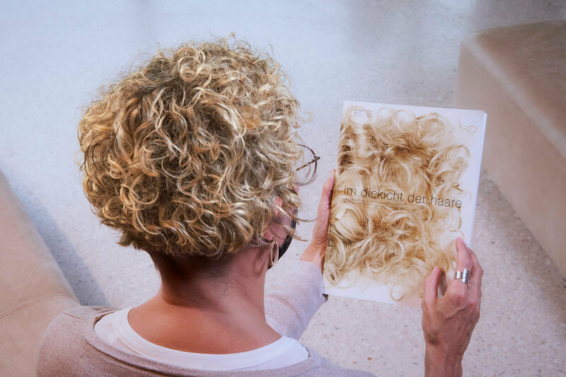 GRIMMWELT | Sonderausstellung | Publikation Im Dickicht der Haare | Foto: Nikolaus Frank Eine Frau mit blonden Locken hält die Publikation Im Dickicht der Haare.