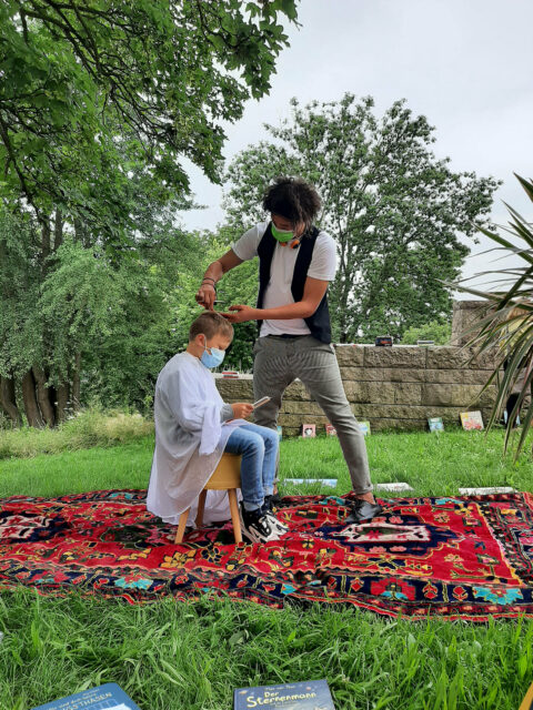 BOOK A LOOK | Vorlesefriseur in der GRIMMWELT Ein Kind bekommt, während es vorliest, die Haare geschnitten.