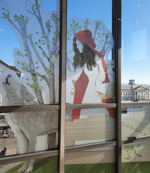 GRIMMWELT zu Gast in der GALERIA | Rotkäppchen-Illustration am Fenster | Illustration: Aliaa Abou Khaddour Blick auf eine Installation von Rotkäppchen, die an den Fensterscheiben von GALERIA befestigt wurde.