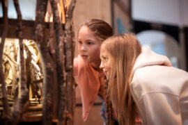 04 | Mechanische Miniaturwelten | IMAGINARIUM | (c) GRIMMWELT Kassel, Foto Nicolas Wefers Zwei Mädchen schauen in einen mechanischen Guckkasten.