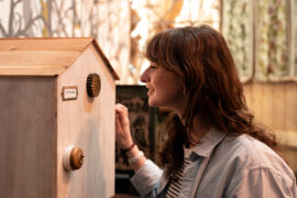 05 | Mechanische Miniaturwelten | IMAGINARIUM | (c) GRIMMWELT Kassel, Foto Nicolas Wefers Besucherin schaut in einem mechanischen Guckkasten.