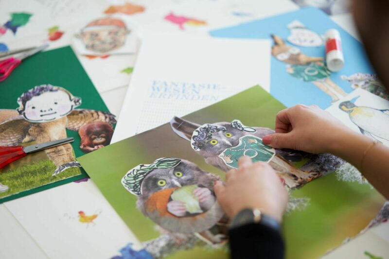 Workshop ERZAEHLENHOEREN | Collage | Foto: Nikolaus Frank Zwei Hände kleben aus Bastelmaterial Fantasiewesen zusammen.