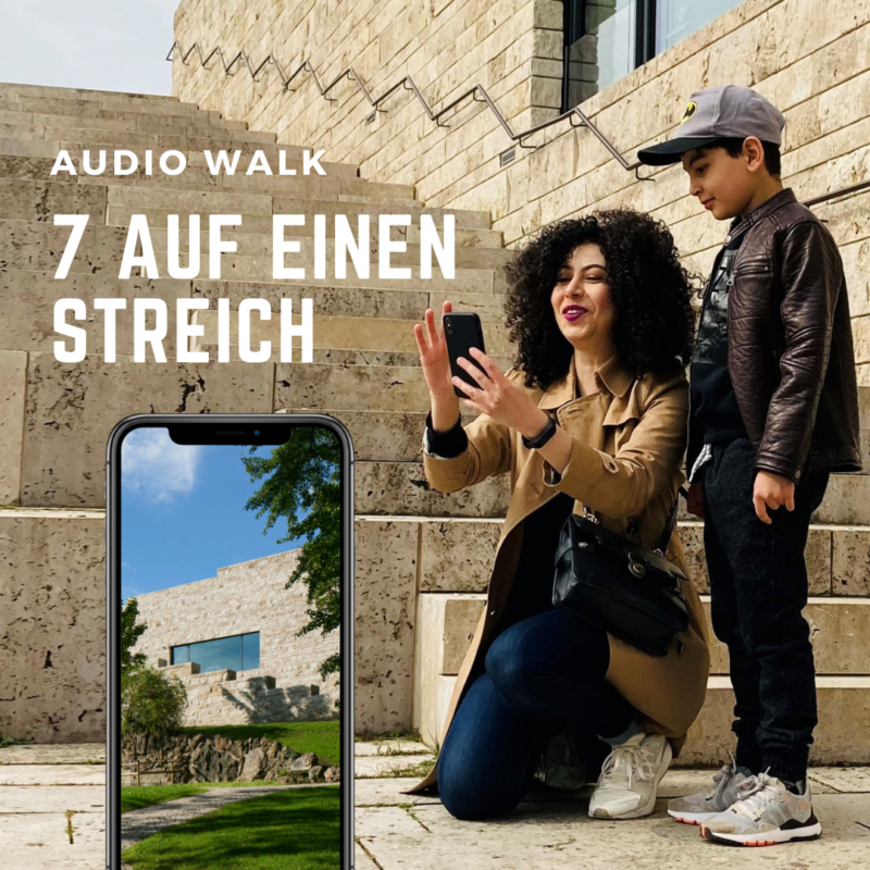 GRIMMWELT | Audiowalk Das Foto zeigt zwei Personen auf den Treppen der GRIMMWELT, die ein Smartphone in der Hand halten. Darauf ist der Audiowalk zu sehen.