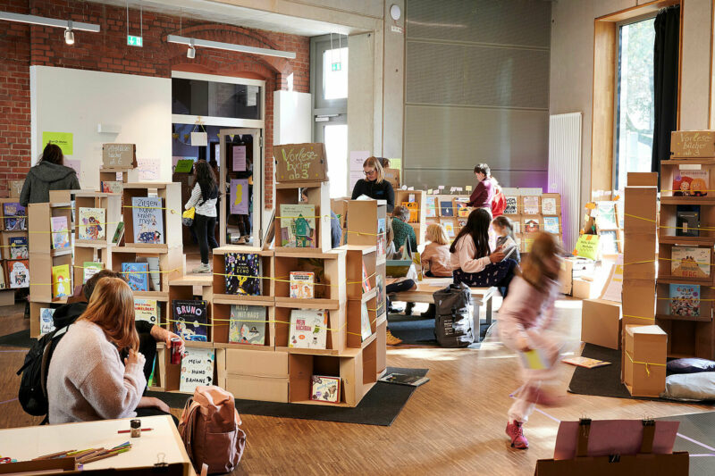 Storytales-Festival in der GRIMMWELT | © Foto Tanja Juergensen Bild zeigt einen Raum mit einer Ausstellung mit Büchern und Kindern und Erwachsenen die lesenund spielen